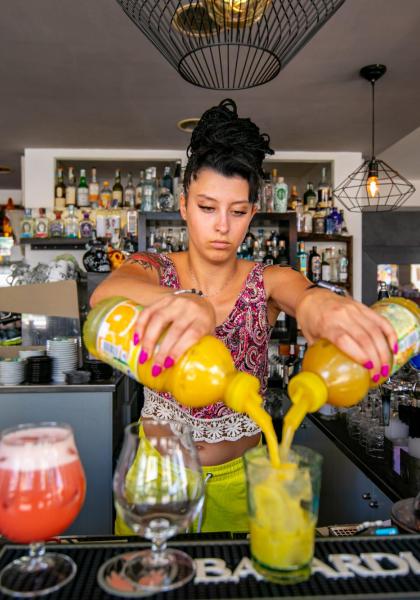 Barista prepara cocktail con due bottiglie, ambiente moderno e accogliente.