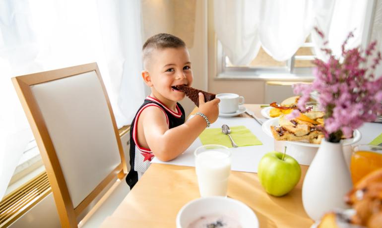 Glückliches Kind isst Kuchen zum Frühstück mit Milch.