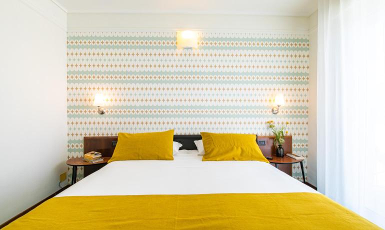 Modern bedroom with yellow pillows and geometric wallpaper.