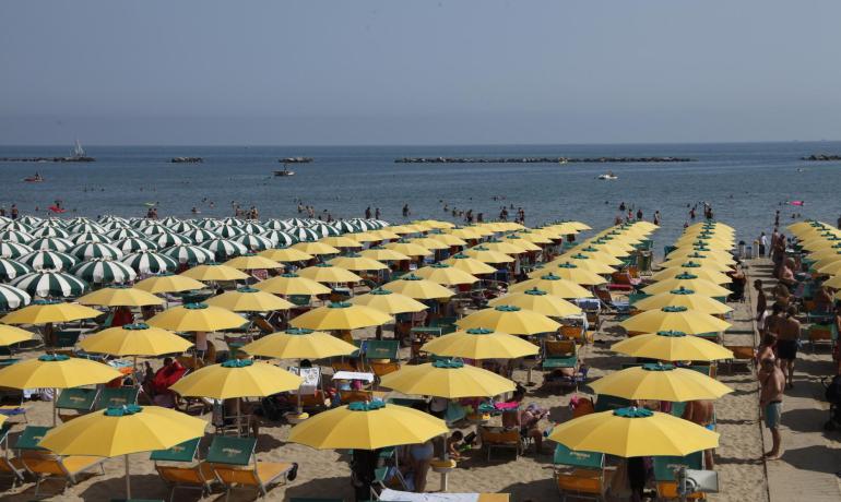 Crowded beach with yellow and green umbrellas, calm sea.