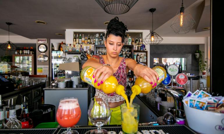 Bartender mixes drinks with two bottles, modern and cozy setting.